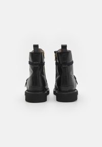 Sorte lær ankle boots med en glat overflade, guld lynlåse og teksturerede såler, der har dekorative stropper og trækstropper bagpå.