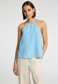 Top halter azzurro chiaro in tessuto trasparente e texturizzato con strisce diagonali. Abbinato a pantaloni larghi color crema.