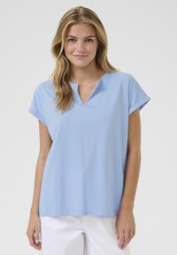 Top V cu mânecă scurtă, de culoare albastru deschis, fabricat din bumbac moale. Croială lejeră cu manșete de mânecă rulate și un tiv curat. Design simplu.