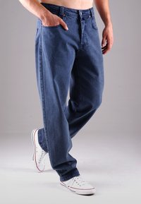 Blaue Denim-Jeans mit entspannter Passform, fünf Taschen, Knopfverschluss und dezenten Nahtdetails. Kombiniert mit weißen Sneakers.