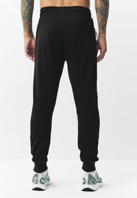Schwarze Jogginghosen aus weichem Stoff mit einem elastischen Bund und Knöchelbündchen, mit einem schmalen Schnitt und seitlichen Taschen.