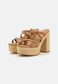 Sandalias de plataforma en tono marrón claro con tacones gruesos trenzados y múltiples tiras acolchadas sobre el pie, sobre un fondo blanco.