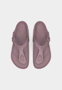 Ζευγάρι σανδάλια χρώματος μοβ με λουρίδα τύπου στρινγκ, ρυθμιζόμενο πόρπη στο πλευρό και διαμορφωμένο πέλμα, εμφανιζόμενα από πάνω σε λευκό φόντο.