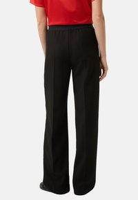 Czarne szerokie spodnie wykonane z lekkiego materiału z elastycznym pasem. Charakteryzują się gładką teksturą i subtelnymi, czystymi liniami.