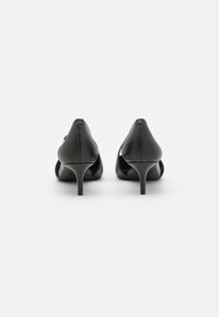 Chaussures à talons hauts noires avec une finition en cuir lisse, bout pointu et talon aiguille étroit, présentant des côtés découpés et un minimalisme dans les détails.