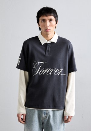 Mörkgrå kortärmad polo med vit krage och ordet "Forever" i kursiv stil. Lager på en ljus långärmad skjorta, tillsammans med denim.