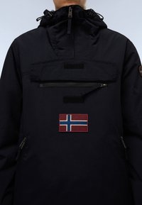 Black anorak jacket with a high collar, front zipper pocket, and a textured Norway flag patch at the chest. Features adjustable hood.