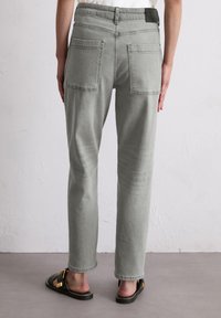 Jeans en denim gris avec une coupe droite, dotés de deux poches arrière et de détails brodés, associés à des sandales à glissière noires.
