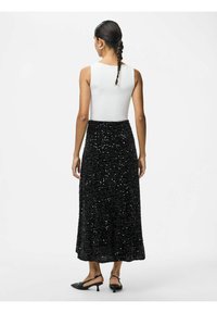 Sort pailetmaxiskirt kombineret med en hvid tætsiddende top, der har en glat tekstur og et svajet design, båret med sorte hæle mule sandaler.