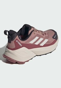Scarpa da trekking Adidas Terrex in rosa e bordeaux, con un upper texturizzato, suola imbottita, dettagli neri e le tre strisce bianche in evidenza.