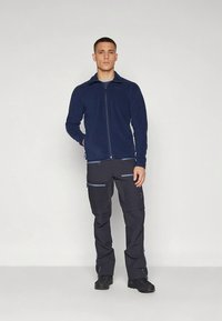 Tumesinine fliisist jope täislukuga ja kõrge kraega, millele on lisatud tumedad püksid mitme tõmblukuga taskuga ning kontrastsete siniste detailidega.