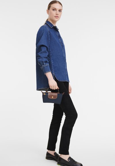 Denim shirt, long sleeves, blue color; black slim-fit pants; small navy bag with brown accents; black loafers with green soles.