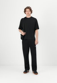 Sort kortærmet t-shirt i afslappet pasform, parret med sorte cargo-bukser med store lommer og et lille logo-patch. Sorte sneakers fuldender looket.