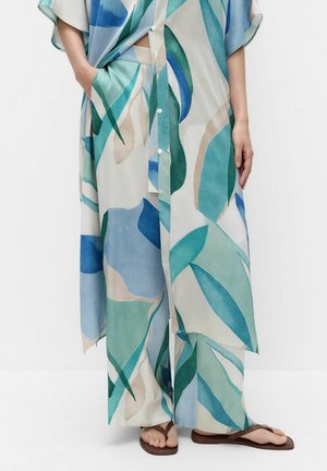 Pantalon large et chemise longue boutonnée assortie avec des motifs abstraits de feuilles bleues et vertes, associée à des sandales marron type tongs.