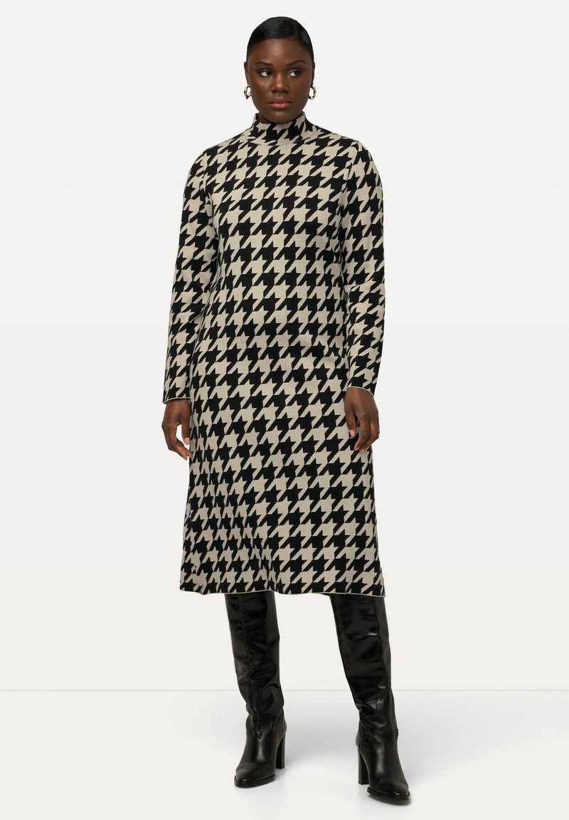 Abito a maniche lunghe con collo a lupetto, caratterizzato da un motivo a scacchi nero e beige. Abbinato a stivali neri al ginocchio per un contrasto elegante.