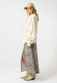 Pulover bej cu textul "SAVVY", asociat cu o fustă midi cu imprimeu leopard, având o fante laterală, și botine ankel de nuanță deschisă.