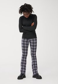 Czarny longsleeve połączony z dopasowanymi spodniami w kratę w odcieniach czerni, bieli i purpury, podkreślonymi krojem bootcut. Czarne botki.