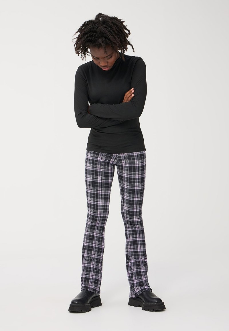 Czarny longsleeve połączony z dopasowanymi spodniami w kratę w odcieniach czerni, bieli i purpury, podkreślonymi krojem bootcut. Czarne botki.