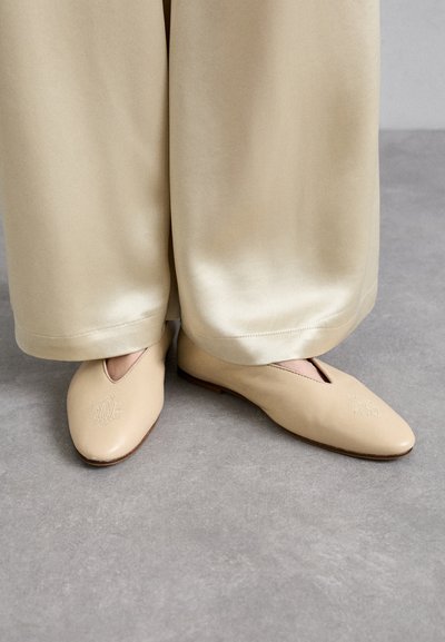 Balerini bej din piele, cu vârful ascuțit, având un design decupat și detalii brodate în față, asortați cu pantaloni largi crem.