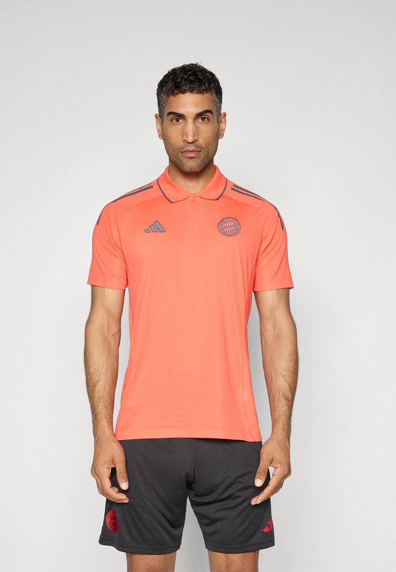 Polo à manches courtes de couleur corail vif avec un col classique et des accents gris, présentant un logo sur la poitrine et des rayures grises sur les épaules.