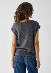 Suéter gris de punto con mangas cortas, dobladillo acanalado y textura suave. Combinado con jeans de mezclilla azul de cintura alta.