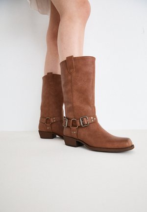 Bruine leren enkellaarzen met een lichtpuntige neus, decoratieve gespen en een lage, gestapelde hak. Glad oppervlak met een matte afwerking.