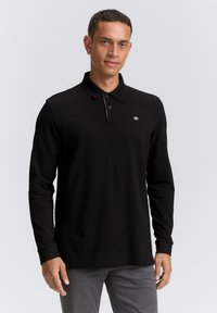 Camisa de polo negra de manga larga con cuello, que cuenta con tres botones y un pequeño logo en el pecho. Material suave y diseño ajustado.