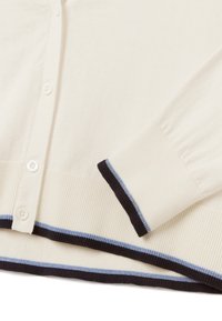 Kremowy sweter robiony na drutach z zapięciem na guziki, ze ściągaczami na dole i przy mankietach, z czarnymi i jasnoniebieskimi paskami jako akcentami.