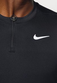 Närbild av en svart Nike sporttröja med blixtlås fram och vit swoosh-logga på bröstet.