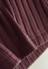 Textil burdeos acanalado con rayas verticales, que presenta una textura suave y detalle de dobladillo, capturando un primer plano del diseño de la tela.