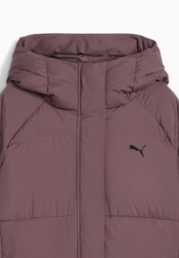 Pufferjakke i støvet mauve med høj krave, sort logo på brystet, quiltet tekstur og et strømlinet design.