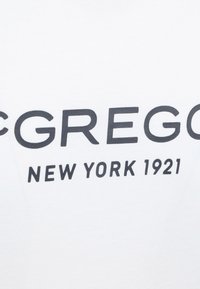 Witte t-shirt met vetgedrukte zwarte tekst: "MCGREGOR NEW YORK 1921" in een schreefloze lettertype, gladde textuur, ontwerp met ronde hals.