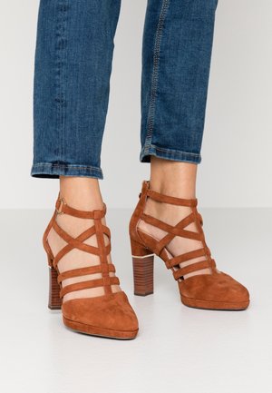 Bruine suède hoge hakken met een puntige neus, voorzien van kruisende strapdetails en een gestructureerde blokhak.