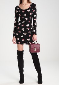 Robe florale noire à manches longues avec des motifs de fleurs blanches et rouges ; associée à un sac à main bordeaux et des bottes noires hautes.