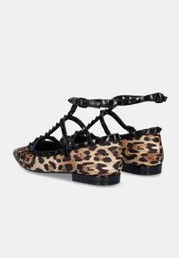 Bailarinas de estampado de leopardo con acentos de charol negro, correas con tachuelas, punta afilada y suela plana. Diseño con cordones en el tobillo.