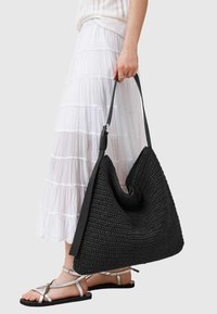Czarna pleciona torba o miękkim kształcie, z g�ładkim czarnym skórzanym paskiem i teksturowaną powierzchnią, w zestawie z białą warstwową spódnicą.