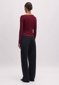Bordeauxfarbener Langarmoberteil mit rundem Halsausschnitt, kombiniert mit hochgeschnittenen schwarzen Marlenehosen. Glatte Stofftextur, lässige Passform.