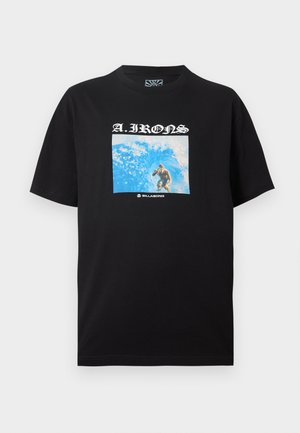 Μαύρο t-shirt με γραφικό σέρφερ που ιππεύει ένα μπλε κύμα, κείμενο "A.IRONS" πάνω και λογότυπο "Billabong" κάτω από την εικόνα.