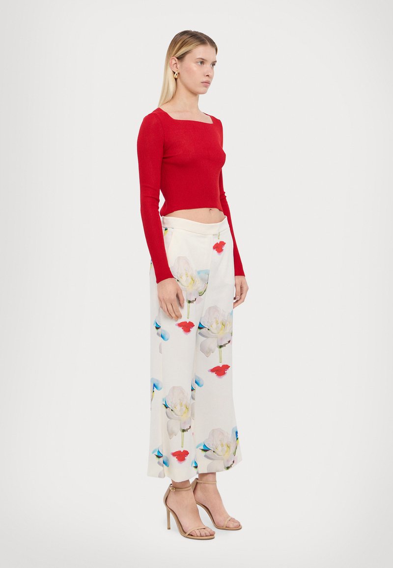 Haut à manches longues rouge à côtes, style court. Pantalon large à motifs floraux en blanc, avec des accents bleus et rouges. Sandales à talons beiges.