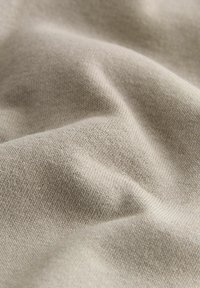 Lys beige stof med en tekstureret, let strækbar overflade, der har et fint strikmønster og en glat, blød finish.