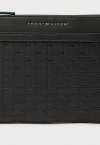 Μαύρο δερμάτινο τσαντάκι χειρός με υφαντό σχέδιο. Διαθέτει πάνω φερμουάρ και ανάγλυφο λογότυπο "TOMMY HILFIGER" στο μπροστινό μέρος.