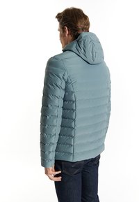 Hooded pufferjacka i mjuk blå, med horisontellt quiltad textur, en figursydd design och elastiska ärmslut, stylet med mörka jeans.