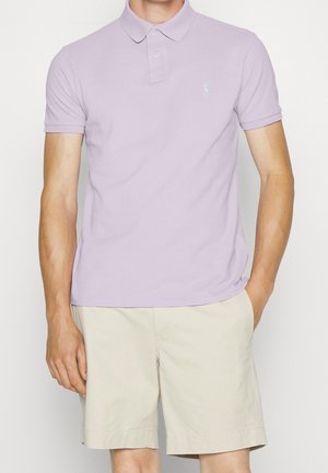 Lila polo shirt met een kraag en korte mouwen. Voorzien van een klein geborduurd logo op de borst. Draagt met lichtbeige shorts.