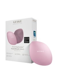 Rosa silikon ansiktsborste med en slät, oval form, placerad bredvid en vit låda med produktinformation och logotyper. Texten på borsten inkluderar en fin textur.
