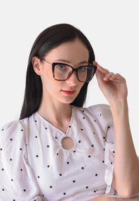 Occhiali rettangolari oversize neri e tartarugati con lenti trasparenti. Il modello indossa una maglia bianca con pois neri e un taglio circolare.