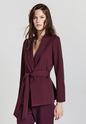 Burgunderfarbener Blazer mit langen Ärmeln, eingekerbten Revers und einem Gürtel in der Taille. Verfügt über zwei Fronttaschen und einen glatten, strukturierten Stoff.