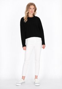 Zwarte cropped kabelgebreide trui, witte slim-fit jeans en witte platform sneakers met zwarte strepen. Eenvoudig, functioneel ontwerp met strakke lijnen.