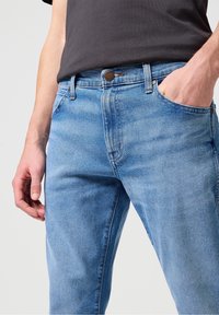 Ljusblå denimjeans med en klassisk design med fem fickor, en bronzfärgad knappstängning och subtila blekningar genom tyget.