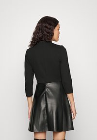 Top noir court à manches trois-quarts, assorti d'une jupe en cuir noir évasée, avec une texture lisse et un détail de fermeture éclair au dos.