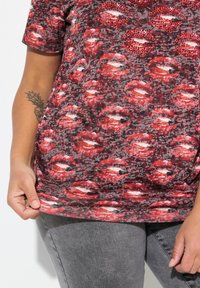Camiseta de manga corta en rojo y gris con un patrón de impresión de labios esparcidos, acentuada por pequeños rhinestones rojos en labios seleccionados.